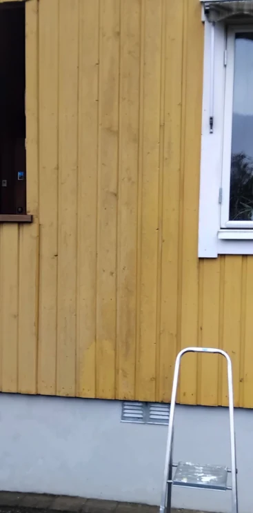 Gulmålad träfasad under pågående fasadtvätt där den tvättade och otvättade ytan syns